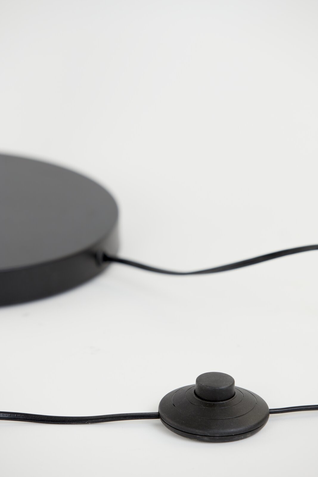 Close-up van de voet van een staande lamp met een zwarte voetschakelaar en kabel, gezien vanaf de zijkant.