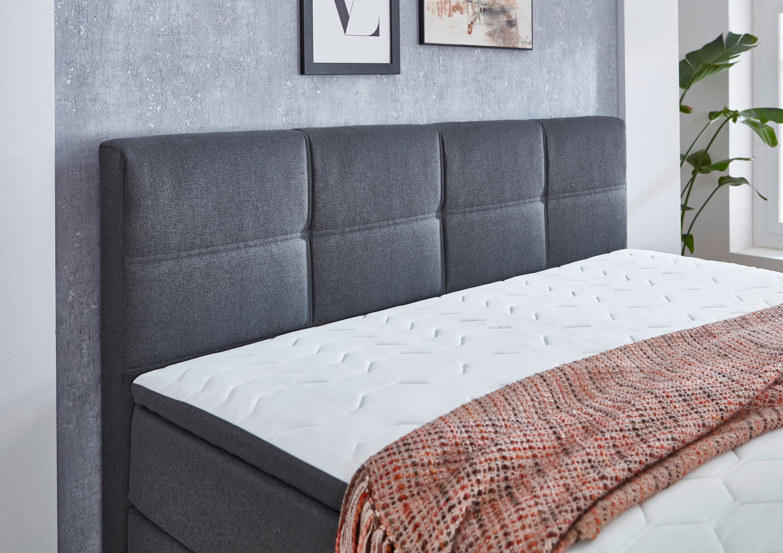 Boxspringbett mit grauem Kopfteil und weißer Matratze, seitliche Perspektive