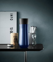 Blauer Impulse Isolierbecher 0,35l mit schwarzem Deckel, frontal auf einem Tisch mit Büroaccessoires.