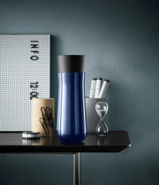 Blauer Impulse Isolierbecher 0,35l mit schwarzem Deckel, frontal auf einem Tisch mit Büroaccessoires.