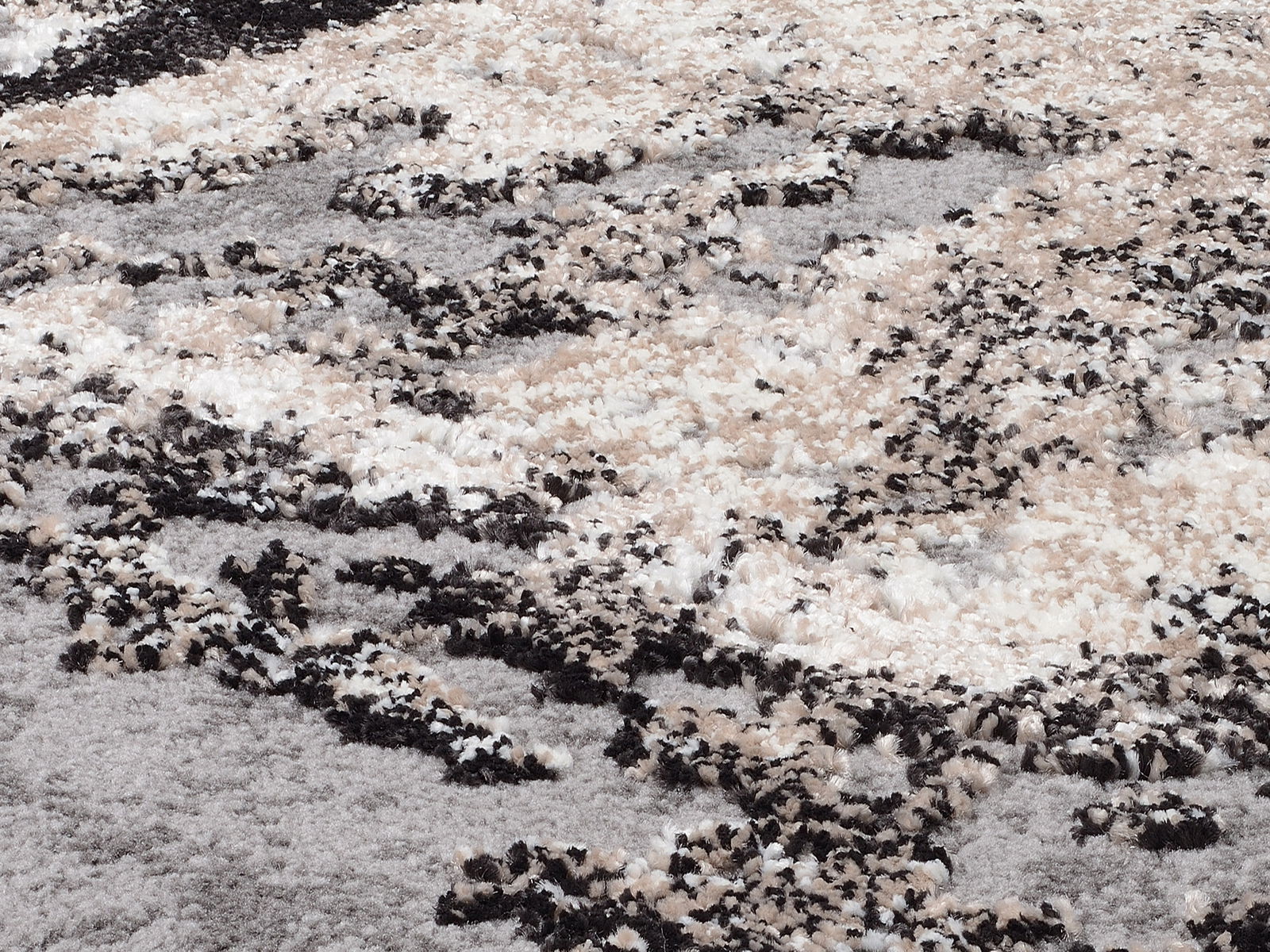 Nahaufnahme eines flauschigen Teppichs mit abstraktem Muster in Beige-, Grau- und Schwarztönen, von oben betrachtet.