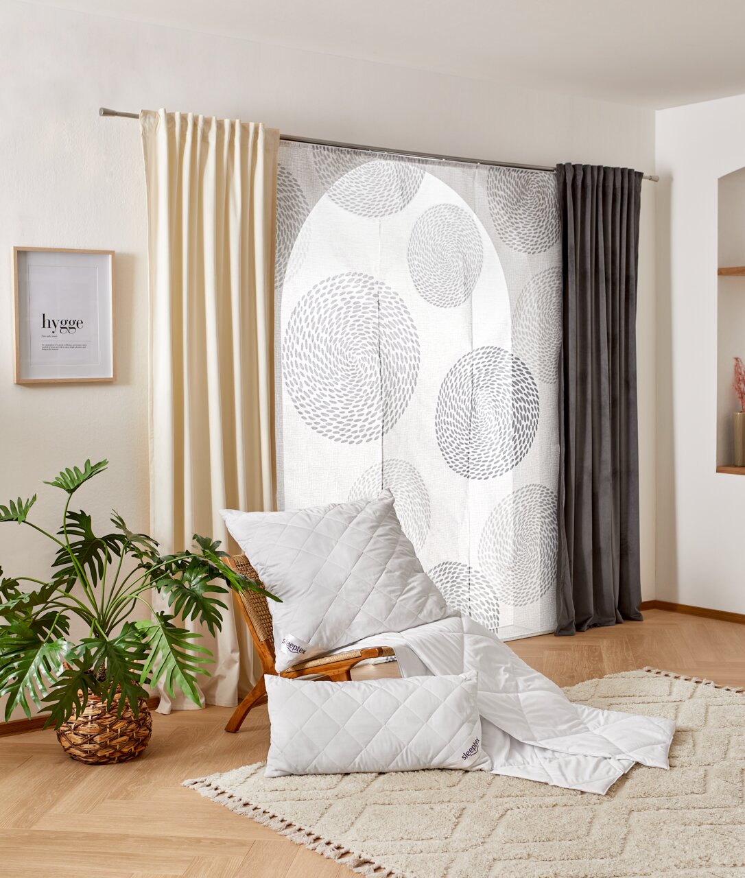 Gemütliches Schlafzimmer mit einem weißen Sommerbett-Set von Sleeptex, bestehend aus einer Decke und einem Kissen, auf einem Stuhl drapiert. Im Hintergrund sind Vorhänge und eine Pflanze zu sehen. Perspektive: seitlich.