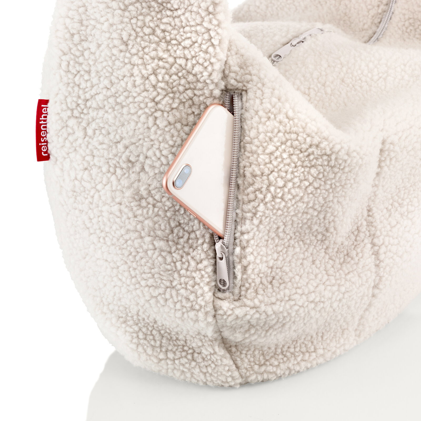 Nahaufnahme einer cremefarbenen Teddy-Fleece-Tasche mit Reißverschlussfach, aus dem ein Smartphone herausragt; Perspektive: seitliche Detailansicht.