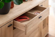 Nahaufnahme eines Holz-Sideboards mit geöffneter Schublade, in der ein rotes Notizbuch und ein Stift liegen. Perspektive von schräg oben.