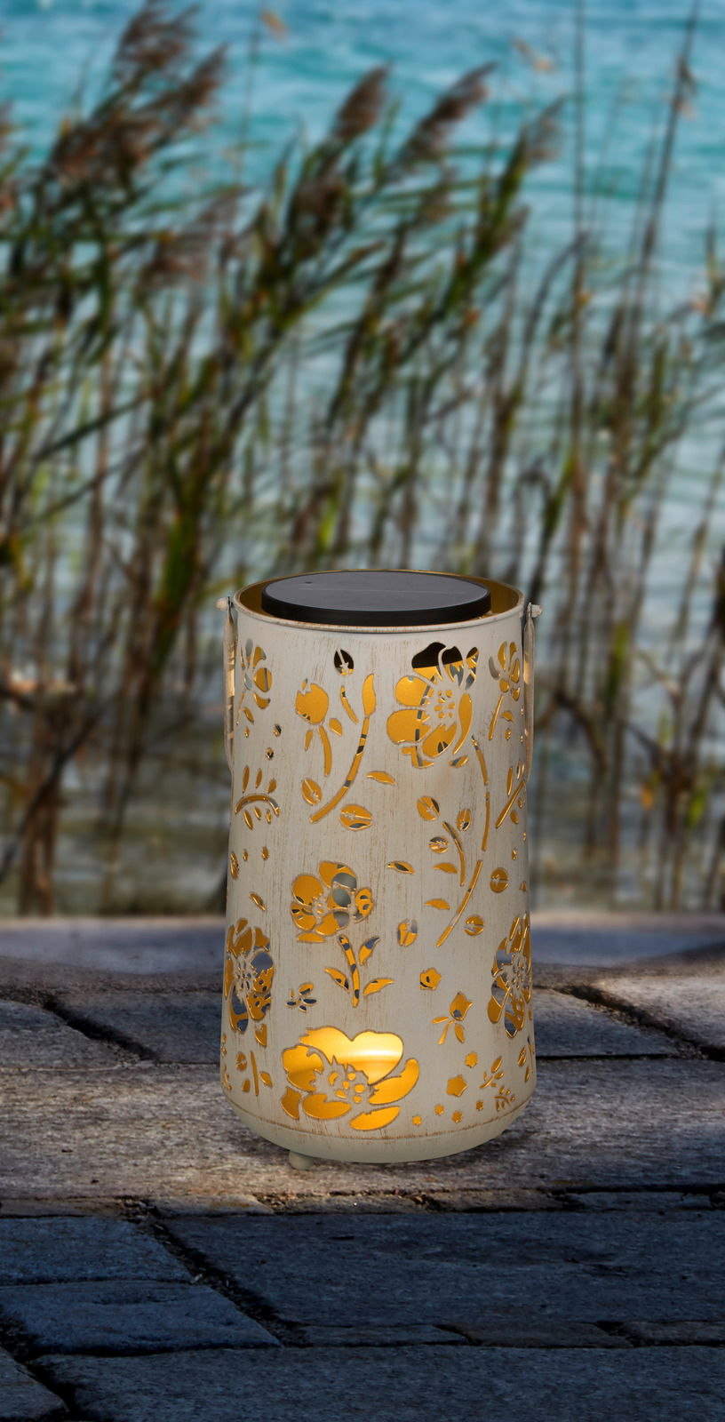 Zurbrüggen LED-Solarleuchte LED-Solarleuchte mit floralem Muster, aufrecht stehend auf einem Steinboden, im Hintergrund Schilf und Wasser.