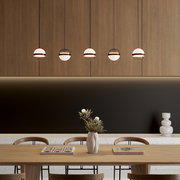 Moderne Pendelleuchten mit kugelförmigen Glas-Schirmen in einer Reihe über einem Esstisch vor Holzvertäfelung; Frontansicht auf Augenhöhe.
