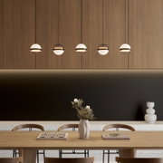 Moderne Pendelleuchten mit kugelförmigen Glas-Schirmen in einer Reihe über einem Esstisch vor Holzvertäfelung; Frontansicht auf Augenhöhe.