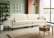 Beiges 3-Sitzer-Sofa mit Stoffbezug und schwarzen Metallfüßen im modernen Wohnzimmer, frontale leicht schräge Perspektive von links; im Hintergrund grüne Wand mit Bildern, Regal und rote Pendelleuchte, rechts Fenster und Couchtisch.