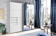 Moderner Schwebetürenschrank mit zwei Türen, eine davon mit Spiegel, in einem hellen Raum mit großen Fenstern und urbanem Ausblick, aus der Perspektive von vorne links.