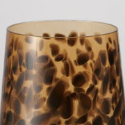 Nahaufnahme eines Trinkglases mit braunem, gepunktetem Muster auf transparentem Hintergrund, Ansicht von oben.