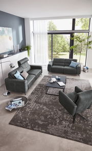 Modernes Wohnzimmer mit zwei dunkelgrauen Sofas und einem Sessel, von oben betrachtet. Große Fenster im Hintergrund lassen viel Licht herein.