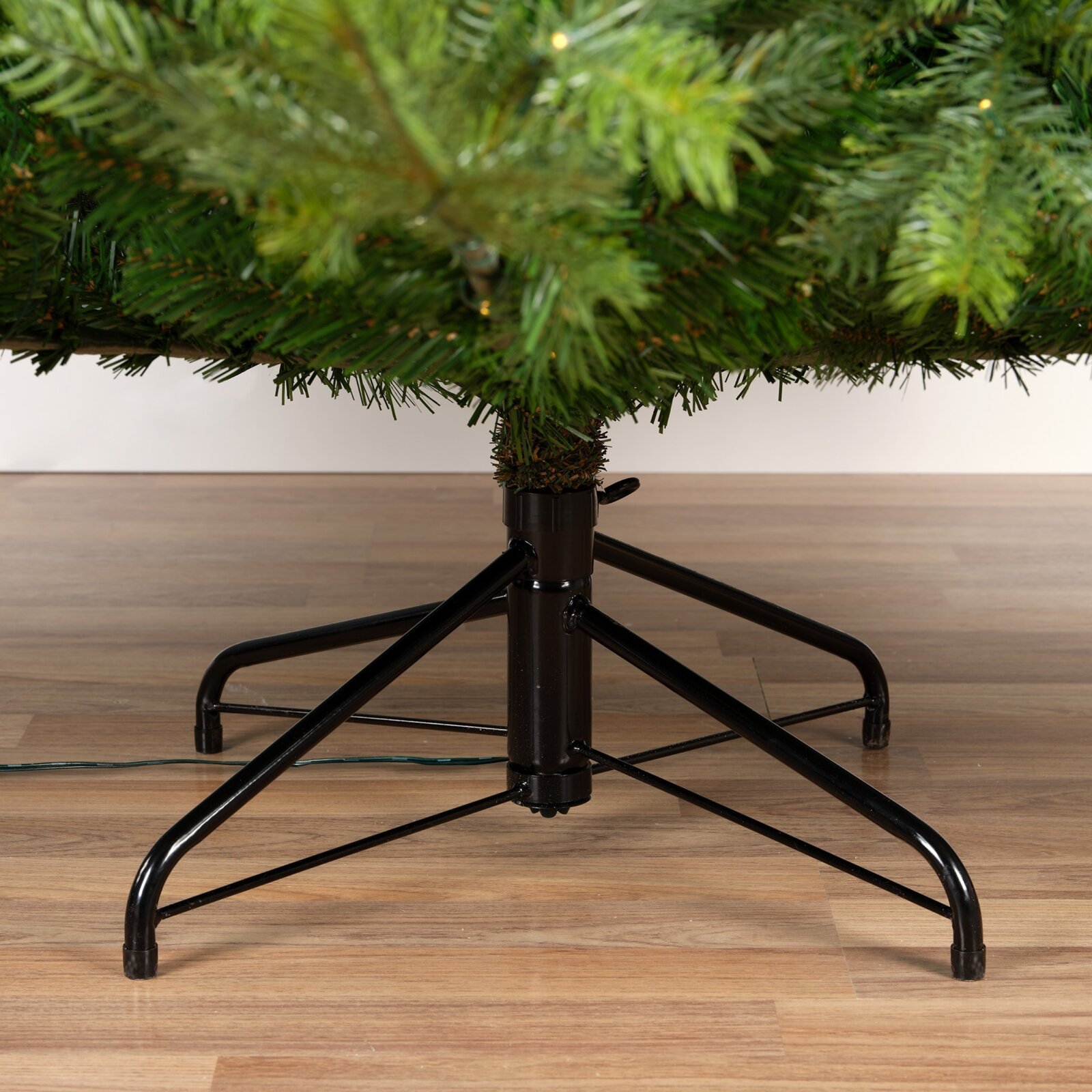 Vooraanzicht van de stevige zwarte metalen standaard van een kunstkerstboom met groene takken en warme verlichting