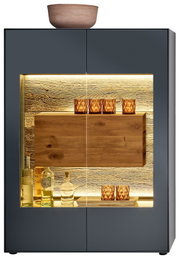 Vooraanzicht van een modern hoogkast met glazen vitrine, verlichte binnenruimte en decoratieve glazen en flessen.