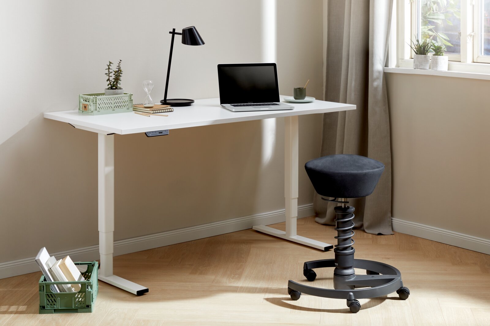 Moderner E-Schreibtisch in einem hellen Raum, ausgestattet mit einem Laptop, einer Lampe und Dekorationen. Perspektive von der Seite.