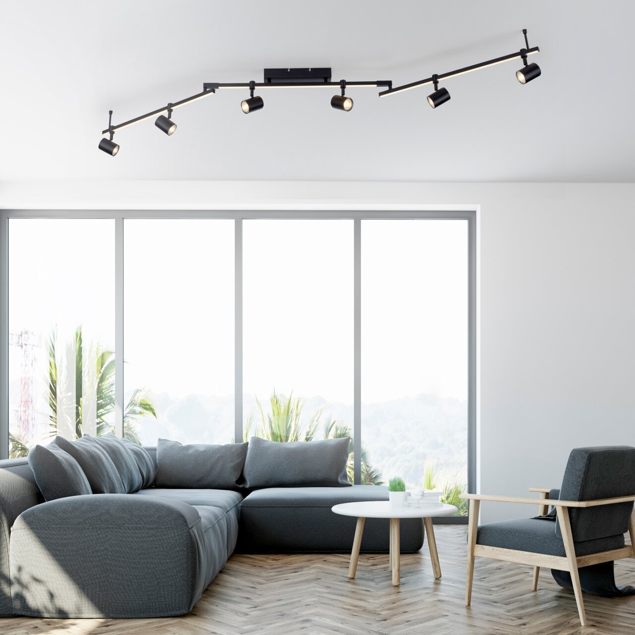 Moderne schwarze Deckenleuchte mit mehreren verstellbaren Strahlern, montiert in einem hellen Wohnzimmer mit großen Fenstern, Blick von unten.