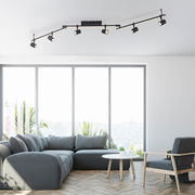 Moderne schwarze Deckenleuchte mit mehreren verstellbaren Strahlern, montiert in einem hellen Wohnzimmer mit großen Fenstern, Blick von unten.