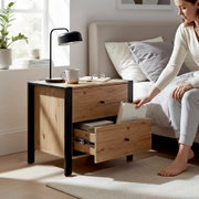 Moderner Nachttisch aus Holz mit schwarzem Metallrahmen und zwei Schubladen neben einem Bett, eine Schublade geöffnet; Ansicht schräg von vorne auf Augenhöhe.