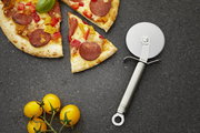 Pizzaschneider aus Edelstahl neben einer angeschnittenen Pizza mit Peperoni und Paprika, von oben betrachtet.