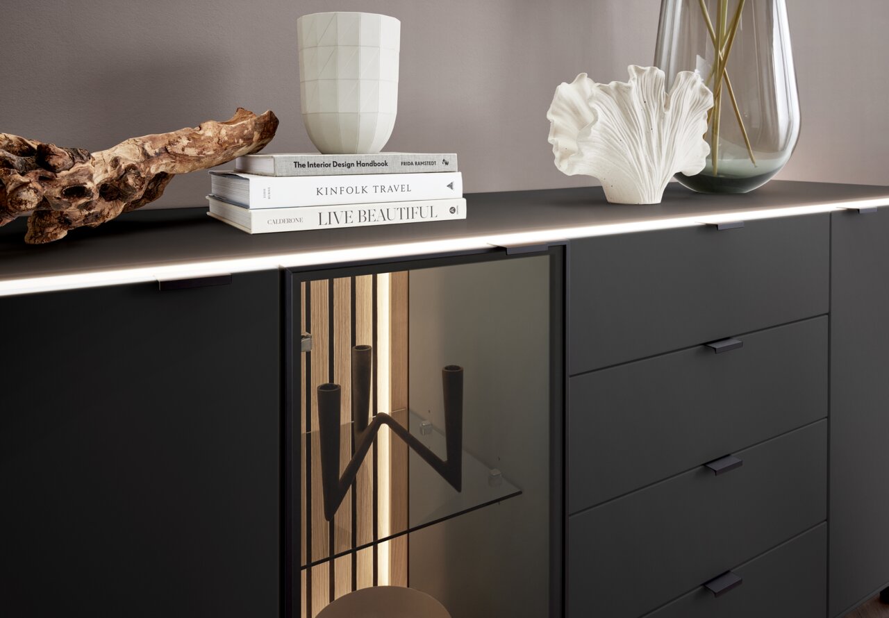 Modernes Sideboard in dunklem Design mit dekorativen Elementen und Büchern auf der Oberseite, seitliche Perspektive.