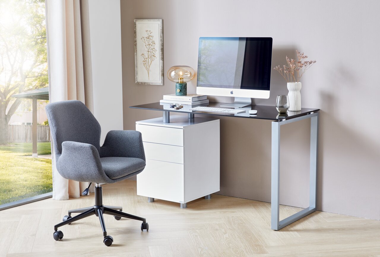 Moderner Schreibtisch mit Glasplatte und Metallrahmen, ausgestattet mit einem weißen Rollcontainer und einem grauen Bürostuhl, seitliche Perspektive.