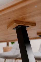 Nahaufnahme der Unterseite eines Esstisches mit schwarzem Metallbein und Holzplatte, aus der Perspektive von unten.