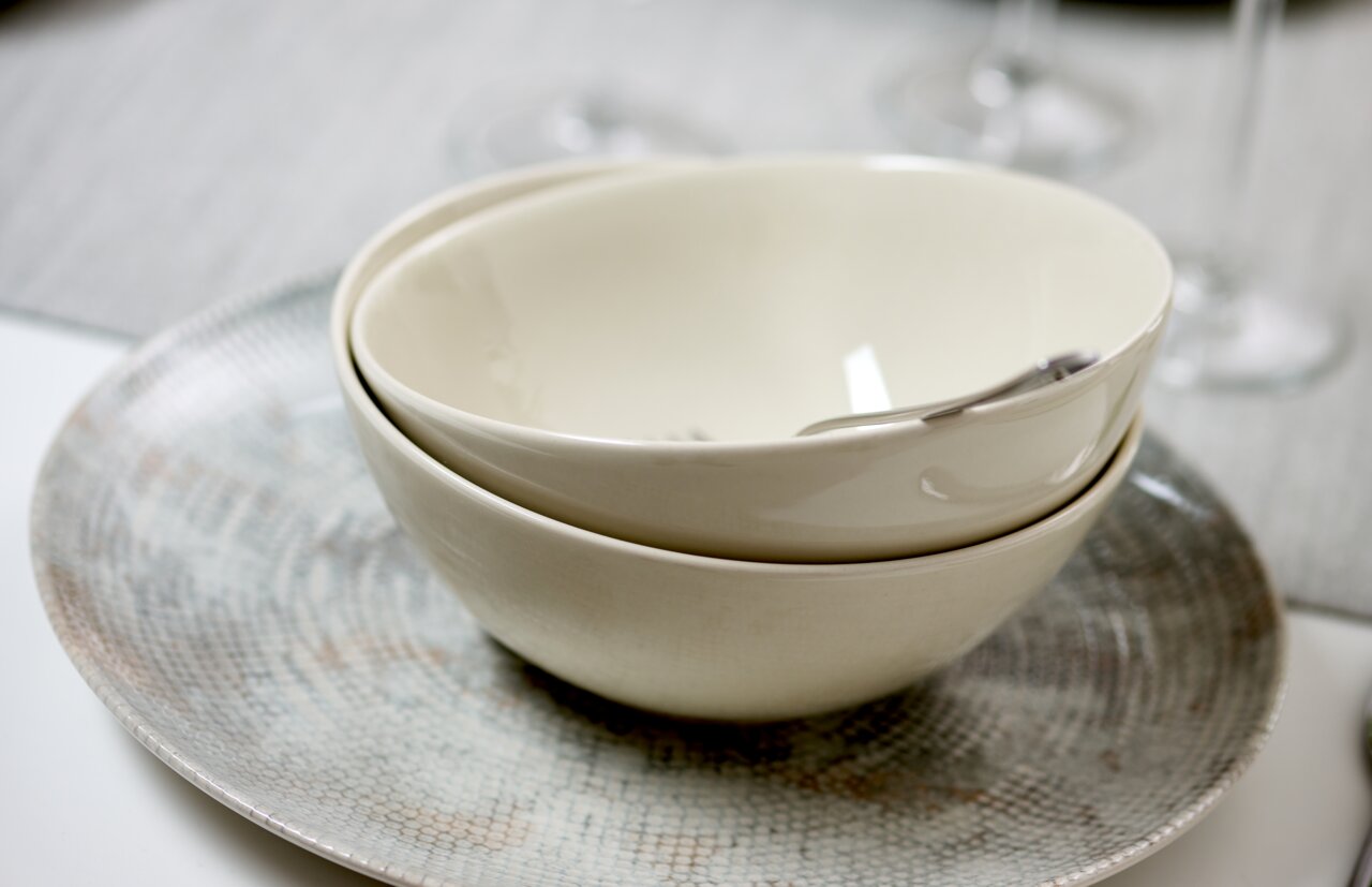 Zwei cremefarbene Schalen gestapelt auf einem flachen, perlmuttfarbenen Teller, seitliche Perspektive.