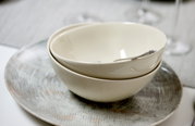 Zwei cremefarbene Schalen gestapelt auf einem flachen, perlmuttfarbenen Teller, seitliche Perspektive.