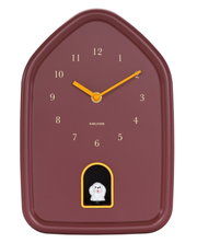 Moderne Wanduhr in Hausform mit braunem Zifferblatt und gelben Zeigern, frontal abgebildet. Unterhalb der 6 befindet sich eine kleine weiße Figur in einem gelben Rahmen.
