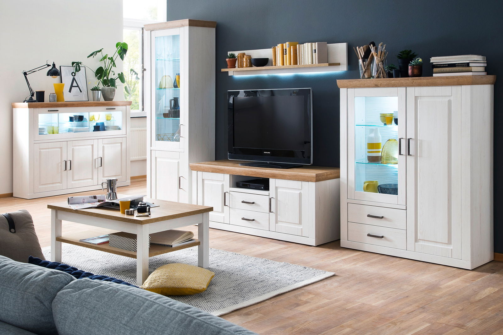 Moderne Wohnzimmer-Wandkombination BREGENZ in heller Holzoptik mit TV-Schrank, Vitrinen und Regalen, aus frontaler Perspektive.