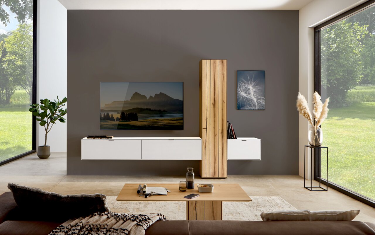 Moderne Wohnzimmer-Wandkombination mit weißem Schrank und Holzelementen, frontal betrachtet. In einem hellen Raum mit großen Fenstern und stilvoller Dekoration.