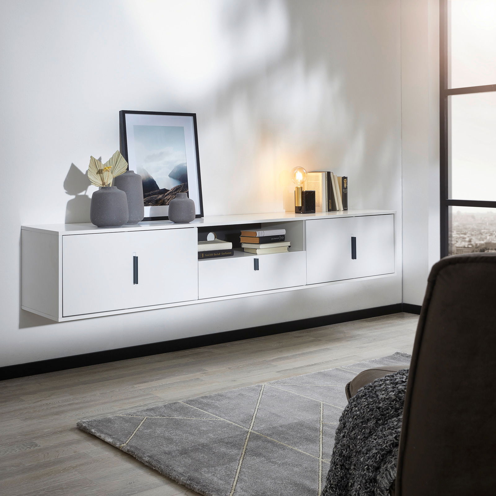 Hom´in TV-Hängeboard ESPADA Modernes weißes TV-Hängeboard mit drei Türen und einem offenen Fach, dekoriert mit Vasen, Büchern und einer Lampe, seitliche Perspektive.