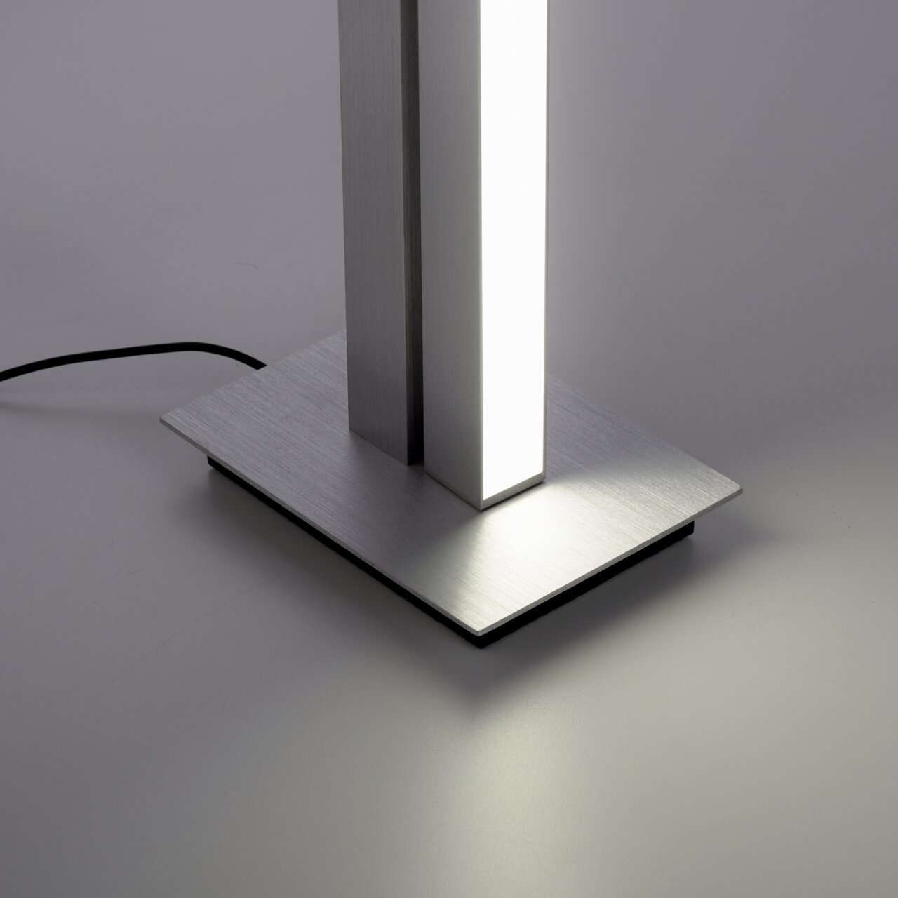 Close-up van de voet van een moderne staande lamp PURE-LINES met een rechthoekige voet van geborsteld metaal en een verlicht verticaal element.