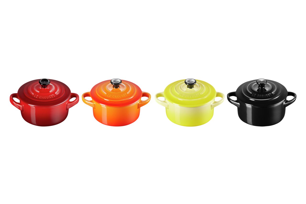 LE CREUSET Mini-Cocotte 4er-Set 10cm FEUER UND FLAMME Vier Mini-Cocottes in verschiedenen Farben (Rot, Orange, Gelb, Schwarz) aus der Vogelperspektive.
