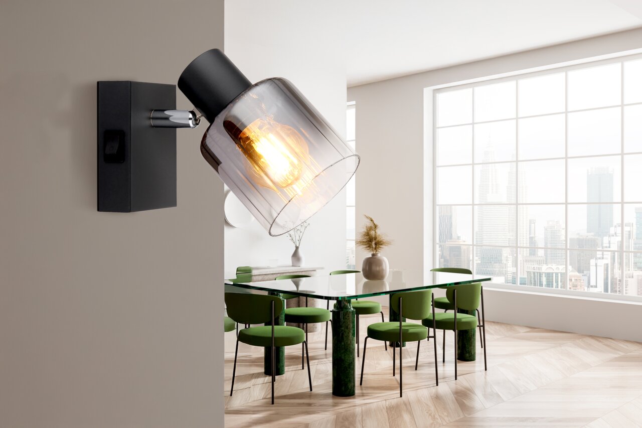 NOWA Strahler JACK Wandstrahler mit modernem Design, schwarzem Gehäuse und transparentem Lampenschirm, seitliche Perspektive in einem hellen Raum mit großen Fenstern.