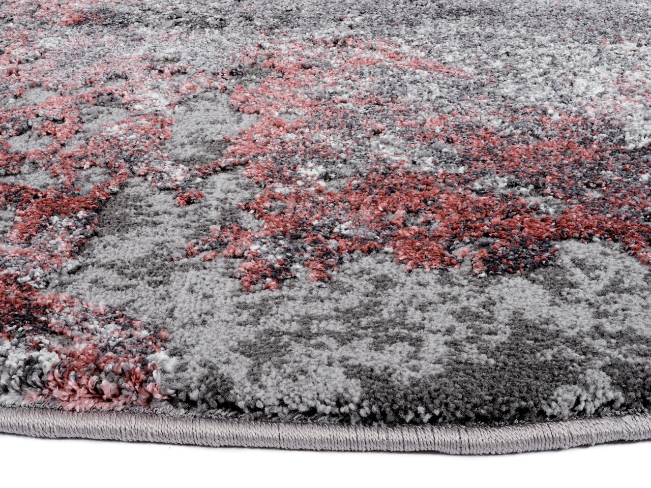 Nahaufnahme eines Designer Teppichs mit grauen und roten Mustern, aus seitlicher Perspektive aufgenommen.