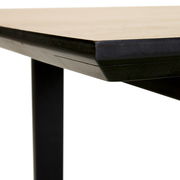 Nahaufnahme der Ecke eines Esstisches mit schwarzem Metallgestell und heller Tischplatte, seitliche Perspektive