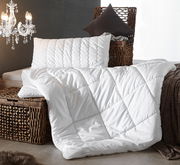 Luxuriöse weiße Faserdecke Duo auf einem geflochtenen Korb, begleitet von einem passenden Kissen, seitliche Perspektive.