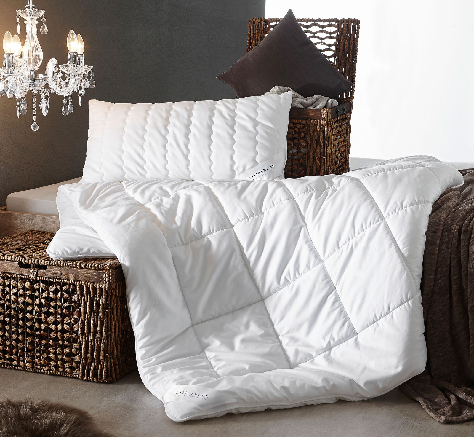 Luxuriöse weiße Faserdecke Duo auf einem geflochtenen Korb, begleitet von einem passenden Kissen, seitliche Perspektive.