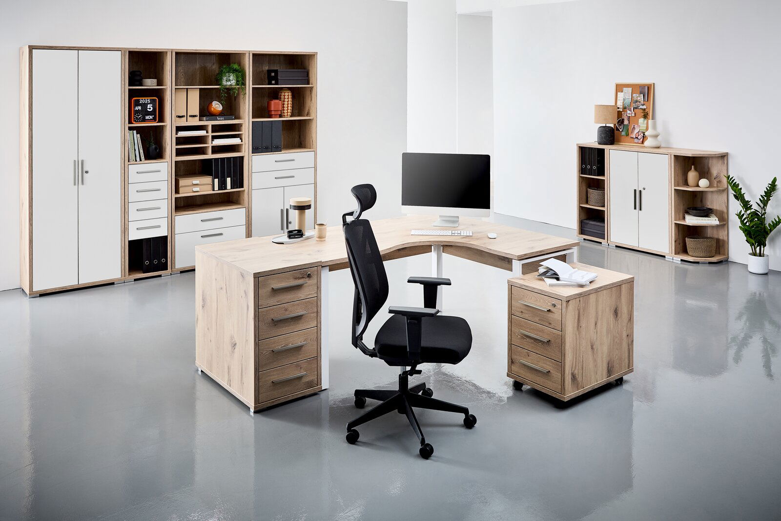 Moderne Büroumgebung mit einem Eckschreibtisch in Holzoptik, umgeben von Regalen und Schränken. Perspektive von vorne links.