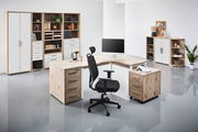 Moderne Büroumgebung mit einem Eckschreibtisch in Holzoptik, umgeben von Regalen und Schränken. Perspektive von vorne links.