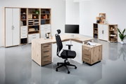 Moderne Büroumgebung mit einem Eckschreibtisch in Holzoptik, umgeben von Regalen und Schränken. Perspektive von vorne links.