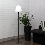 Moderne Stehlampe mit schwarzem Metallfuß und weißem, konischem Lampenschirm in einer Wohnzimmerecke neben großer Zimmerpflanze und Sofa, frontale Perspektive