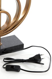 Close-up van een lampvoet met een gebogen, bronskleurig ontwerp en een zwarte kabel met schakelaar en stekker.
