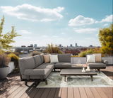 Modernes Lounge-Set auf einer Dachterrasse mit Blick auf die Stadt, bestehend aus einem grauen Ecksofa, einem niedrigen Tisch und dekorativen Kissen, bei Tageslicht fotografiert.