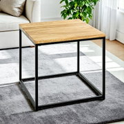 Moderner Beistelltisch mit rechteckiger Holzplatte in Eiche-Optik und schwarzem Metallgestell im Wohnzimmer auf grauem Teppich, schräg von vorne aus leicht erhöhter Perspektive fotografiert