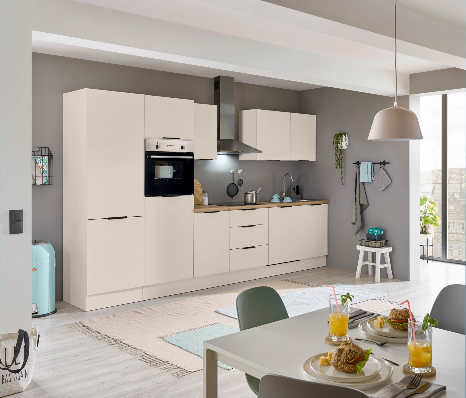 Yourkitchen Kühlschrankumbau 60 MULTAN Moderne Einbauküche in heller Farbe mit integriertem Backofen und Kühlschrank, Dunstabzugshaube und Arbeitsplatte aus Holz. Perspektive von der Seite mit Blick auf den Esstisch im Vordergrund.