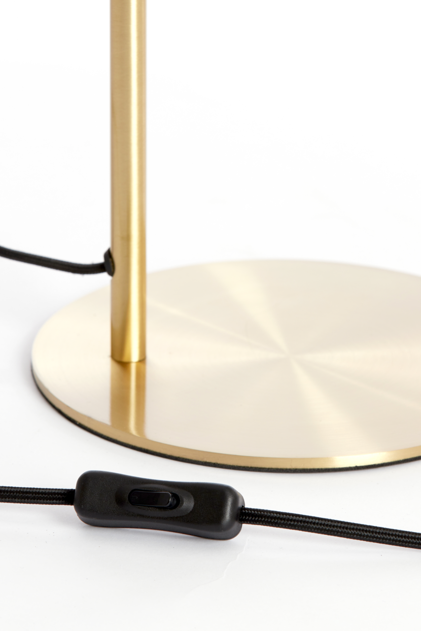 Nahaufnahme einer Tischleuchte mit einem goldenen, runden Sockel und einem schwarzen Kabel mit Schalter, seitliche Perspektive.