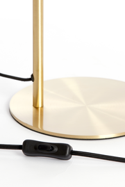 Nahaufnahme einer Tischleuchte mit einem goldenen, runden Sockel und einem schwarzen Kabel mit Schalter, seitliche Perspektive.