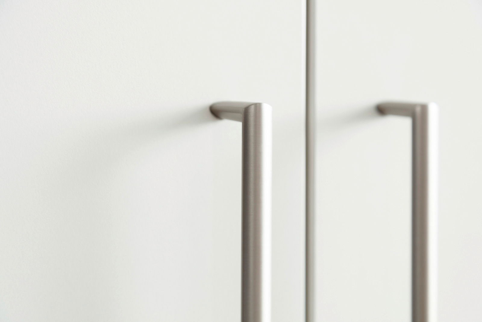 Nahaufnahme von zwei modernen, silbernen Griffen an einer weißen Schranktür, seitliche Perspektive