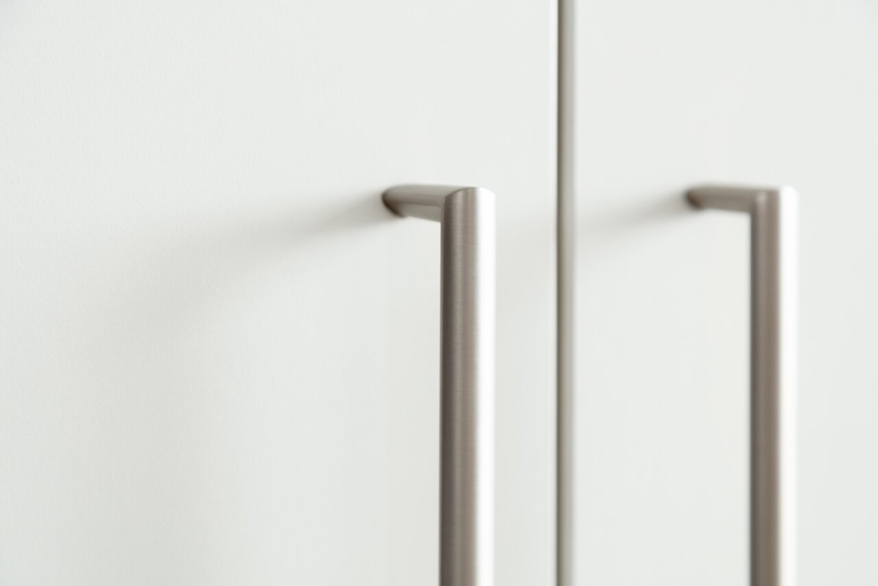 Nahaufnahme von zwei modernen, silbernen Griffen an einer weißen Schranktür, seitliche Perspektive